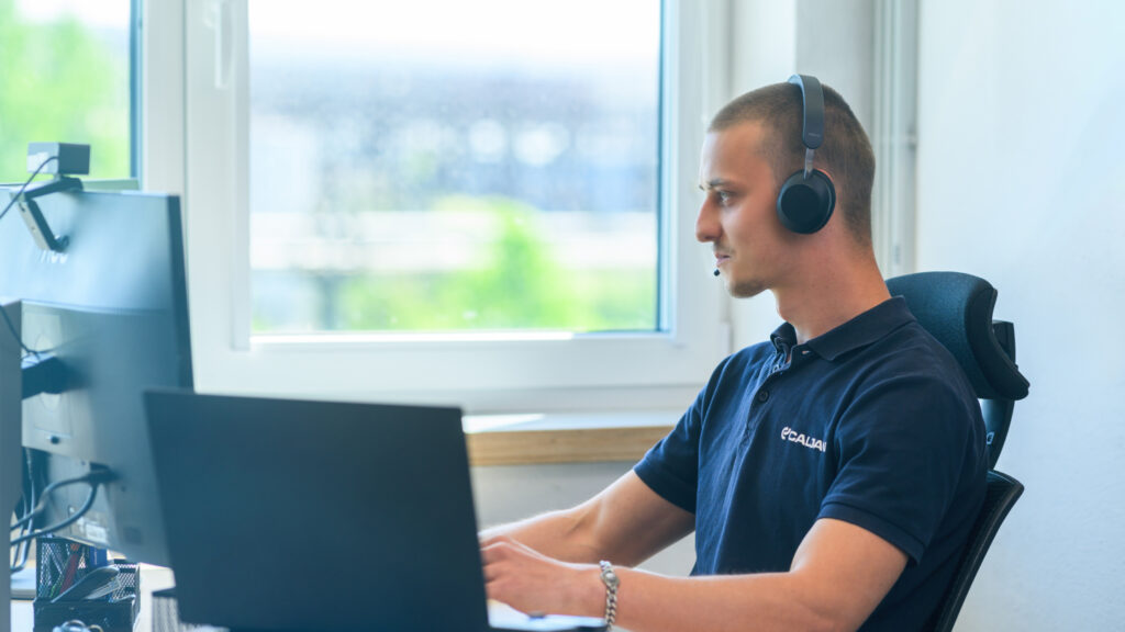 Male Caljan hotline support operator in front of his desk having a call with a client